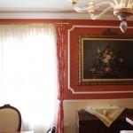 immagine rappresenta una cornice in gesso su parete rossa che adorna un quadro floreale